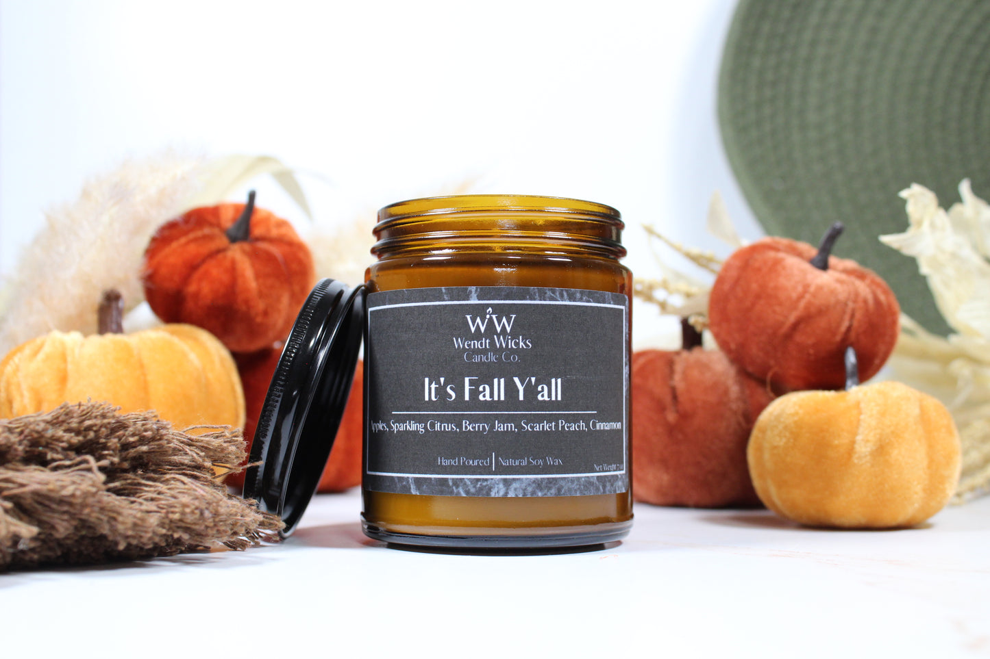 Wendt Wicks amber glass jar candle with black lid leaning on side of candle. Candle labeled 'It's Fall Y'all' with pumpkins and decorative Autumn elements on a white background