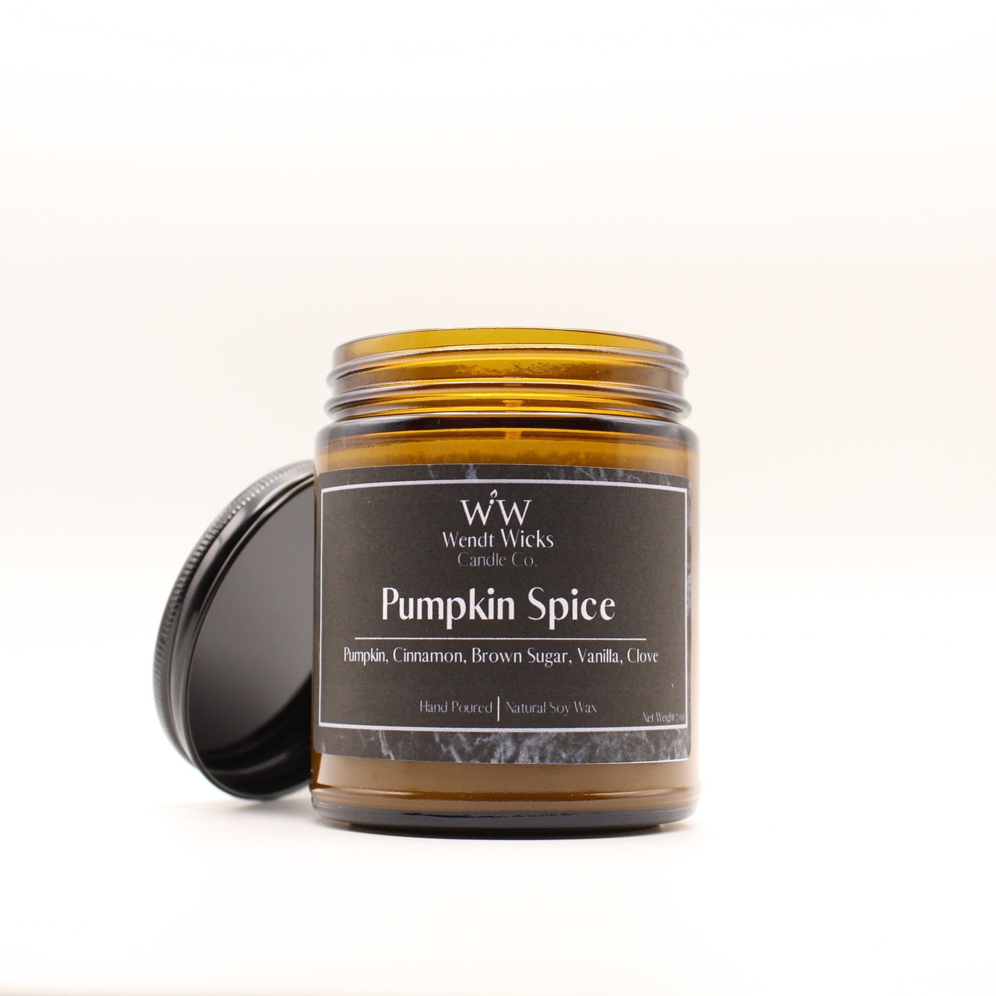 Wendt Wicks amber glass jar candle with black lid leaning against its left side. Candle labeled 'Pumpkin Spice' on a white background