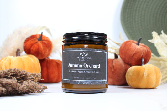 Wendt Wicks amber glass jar candle with black lid. Candle labeled 'Autumn Orchard' with pumpkins and decorative Autumn elements on a white background