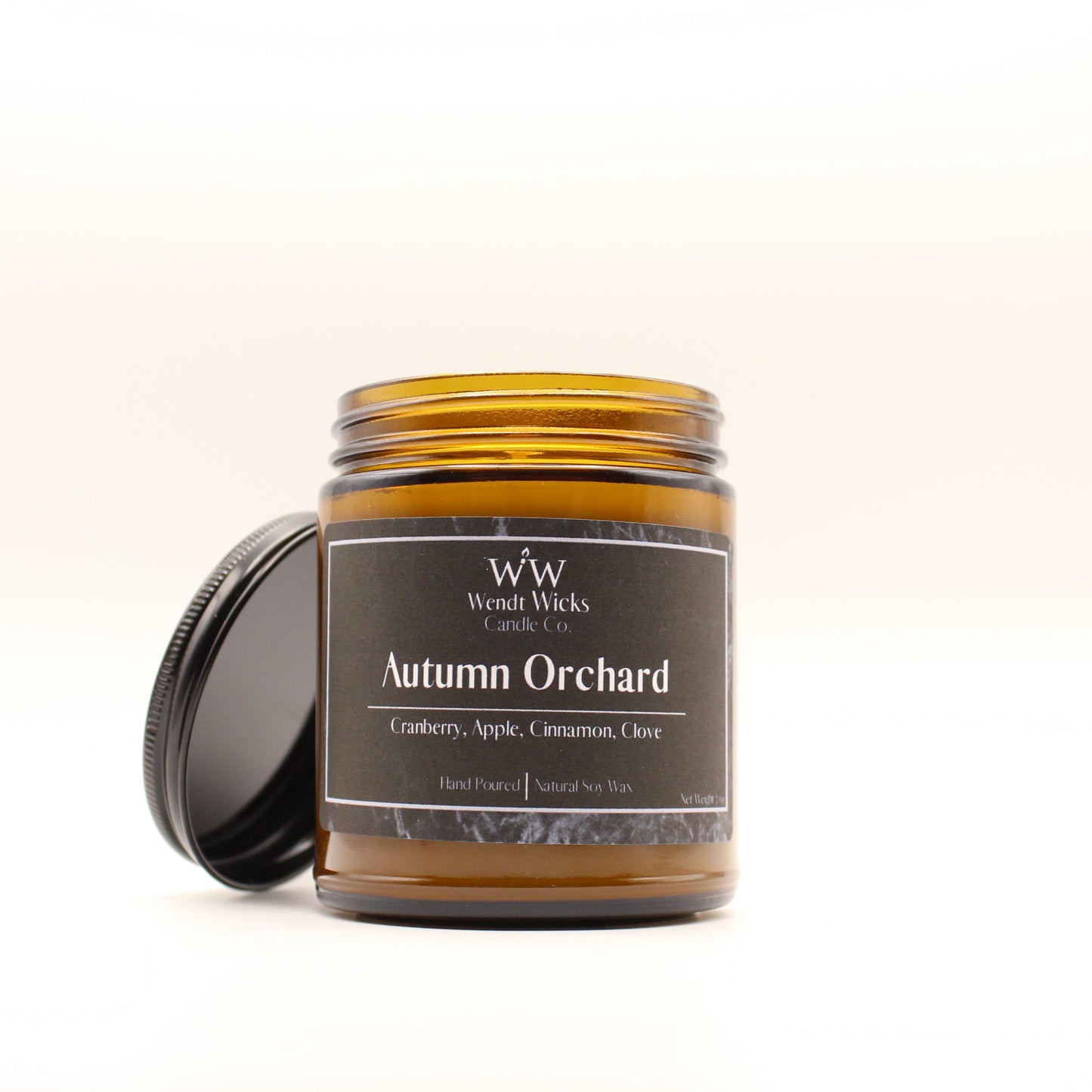 Wendt Wicks amber glass jar candle with black lid leaning against its left side. Candle labeled 'Autumn Orchard' on a white background