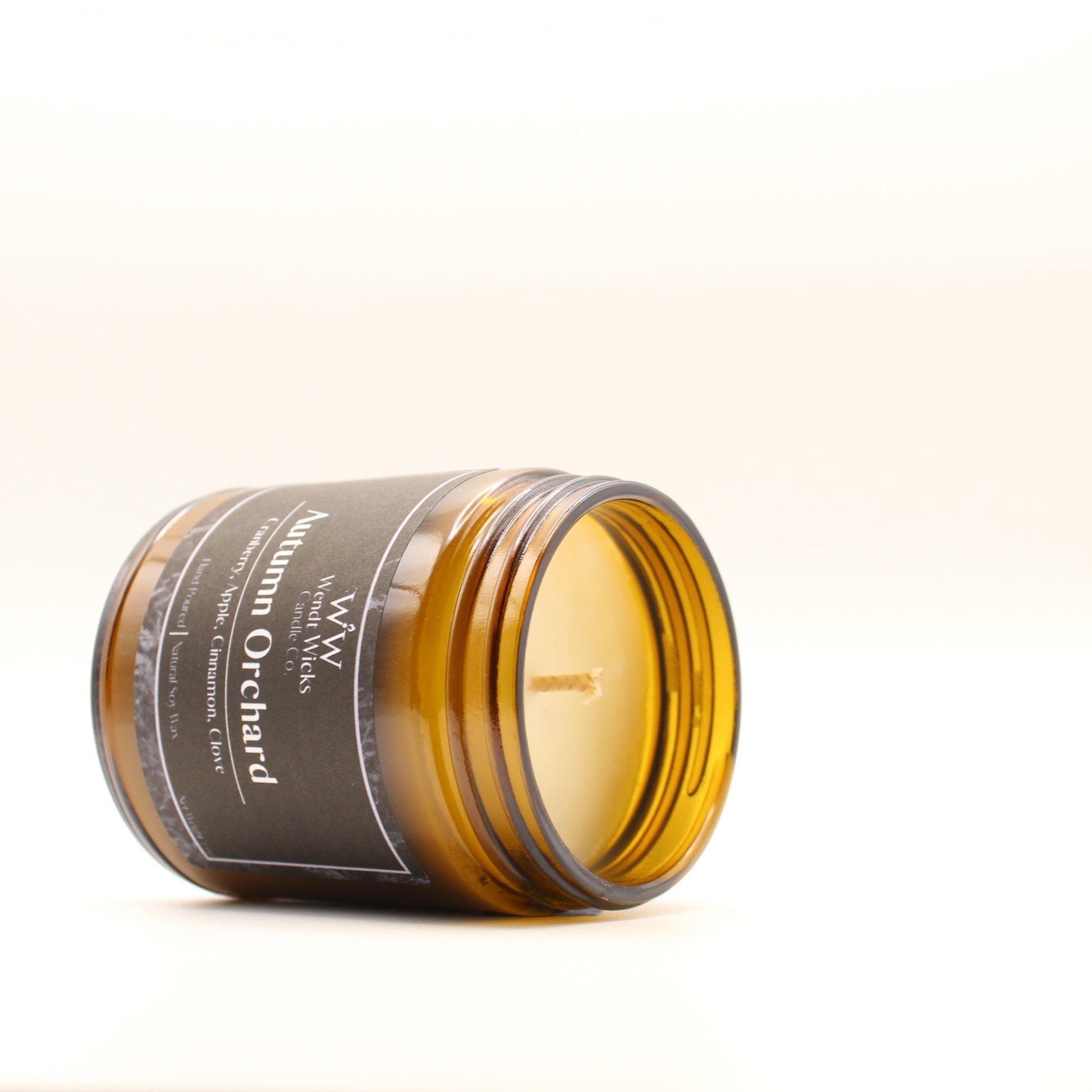 Wendt Wicks amber glass jar candle laying down to showcase wax and cotton wick. Candle labeled 'Autumn Orchard' on a white background