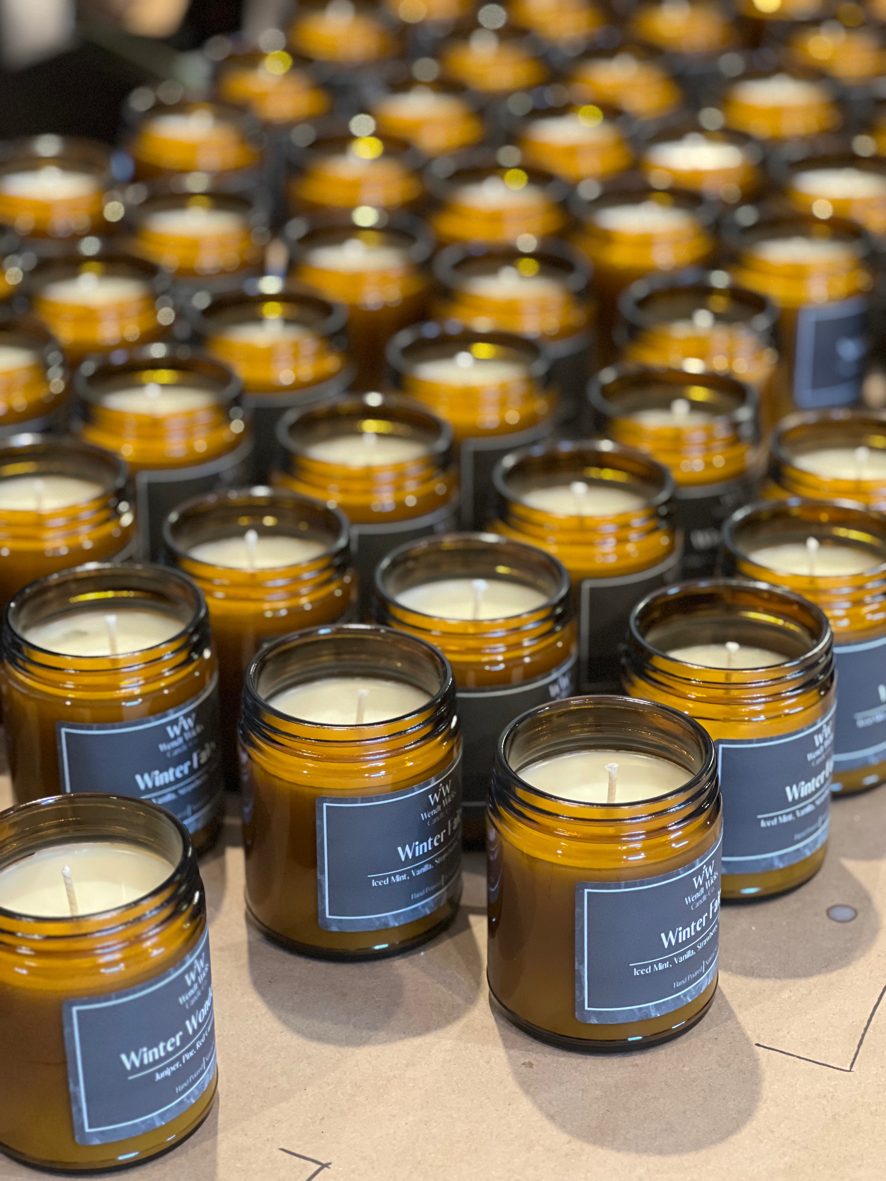 Multiple hand poured amber glass candles with labels on a table