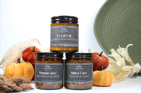 Three Wendt Wicks amber glass jar candles stacked in a pyramid with black lids. Candles labeled 'Pumpkin Spice' 'It's Fall Y'all' and 'Mulled Cider' with pumpkins and decorative Autumn elements on a white background