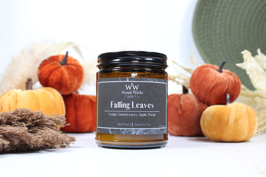 Wendt Wicks amber glass jar candle with black lid. Candle labeled 'Falling Leaves' with pumpkins and decorative Autumn elements on a white background