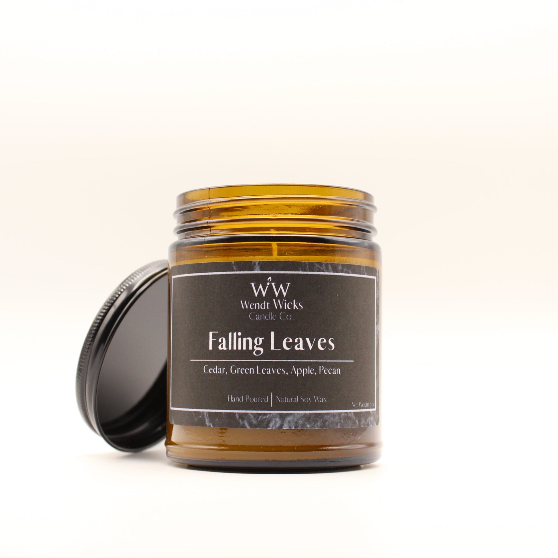 Wendt Wicks amber glass jar candle with black lid leaning on its left side. Candle labeled 'Falling Leaves' on a white background