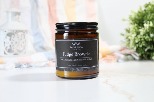 Candle labeled 'Fudge Brownie' by Wendt Wicks on a marble surface with a blurred background.
