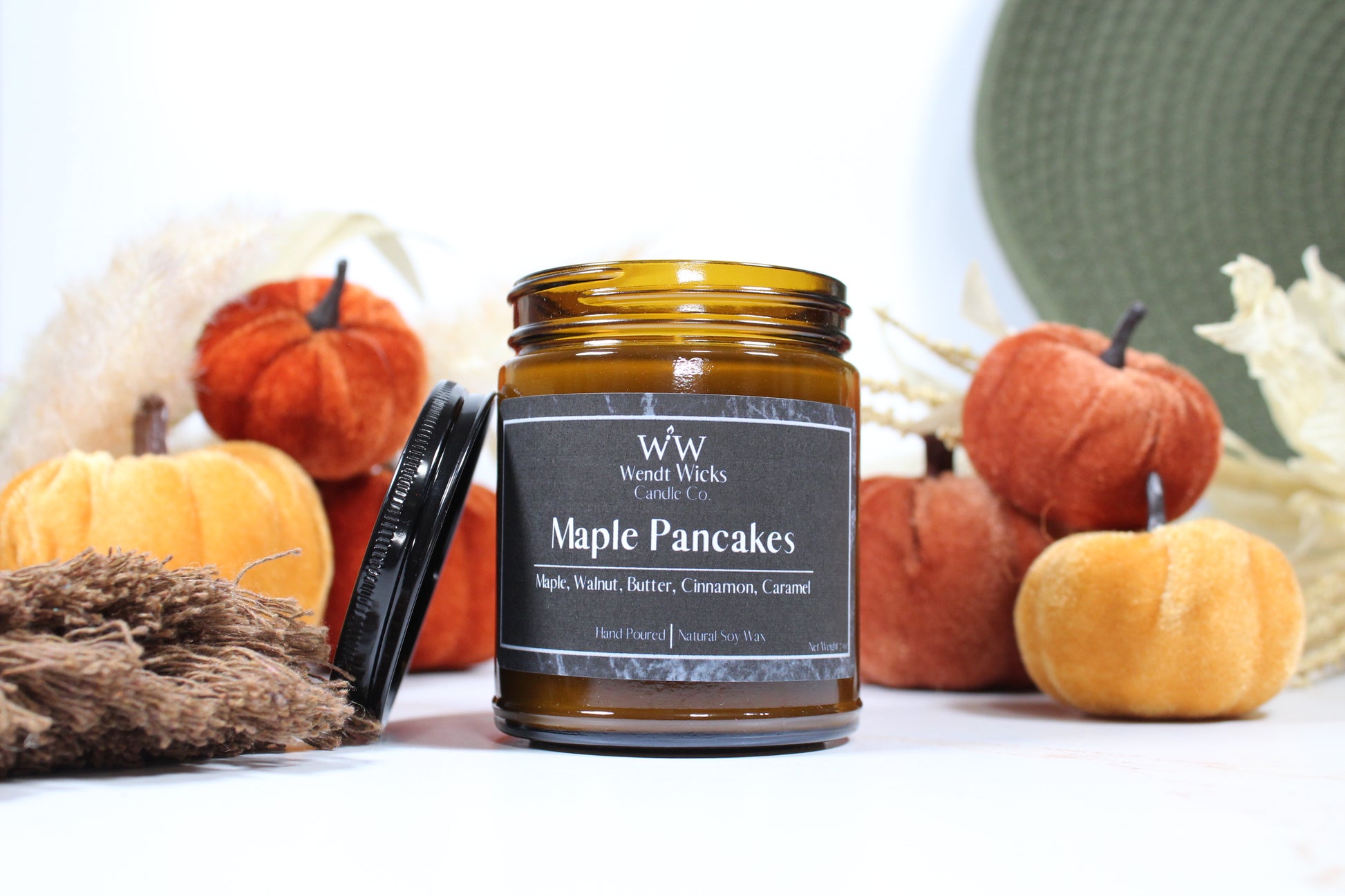 Wendt Wicks amber glass jar candle with black lid leaning on its left side. Candle labeled 'Maple Pancakes' with pumpkins and decorative Autumn elements on a white background
