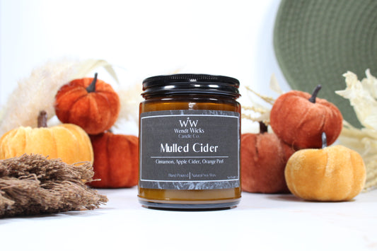 Wendt Wicks amber glass jar candle with black lid. Candle labeled 'Mulled Cider' with pumpkins and decorative Autumn elements on a white background