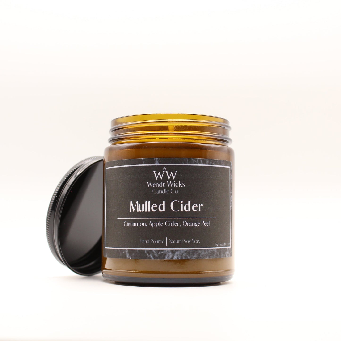 Wendt Wicks amber glass jar candle with black lid leaning against its left side. Candle labeled 'Mulled Cider' on a white background