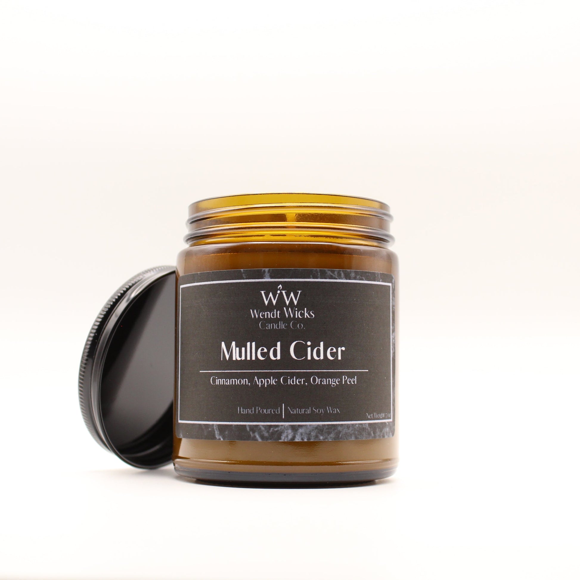 Wendt Wicks amber glass jar candle with black lid leaning against its left side. Candle labeled 'Mulled Cider' on a white background