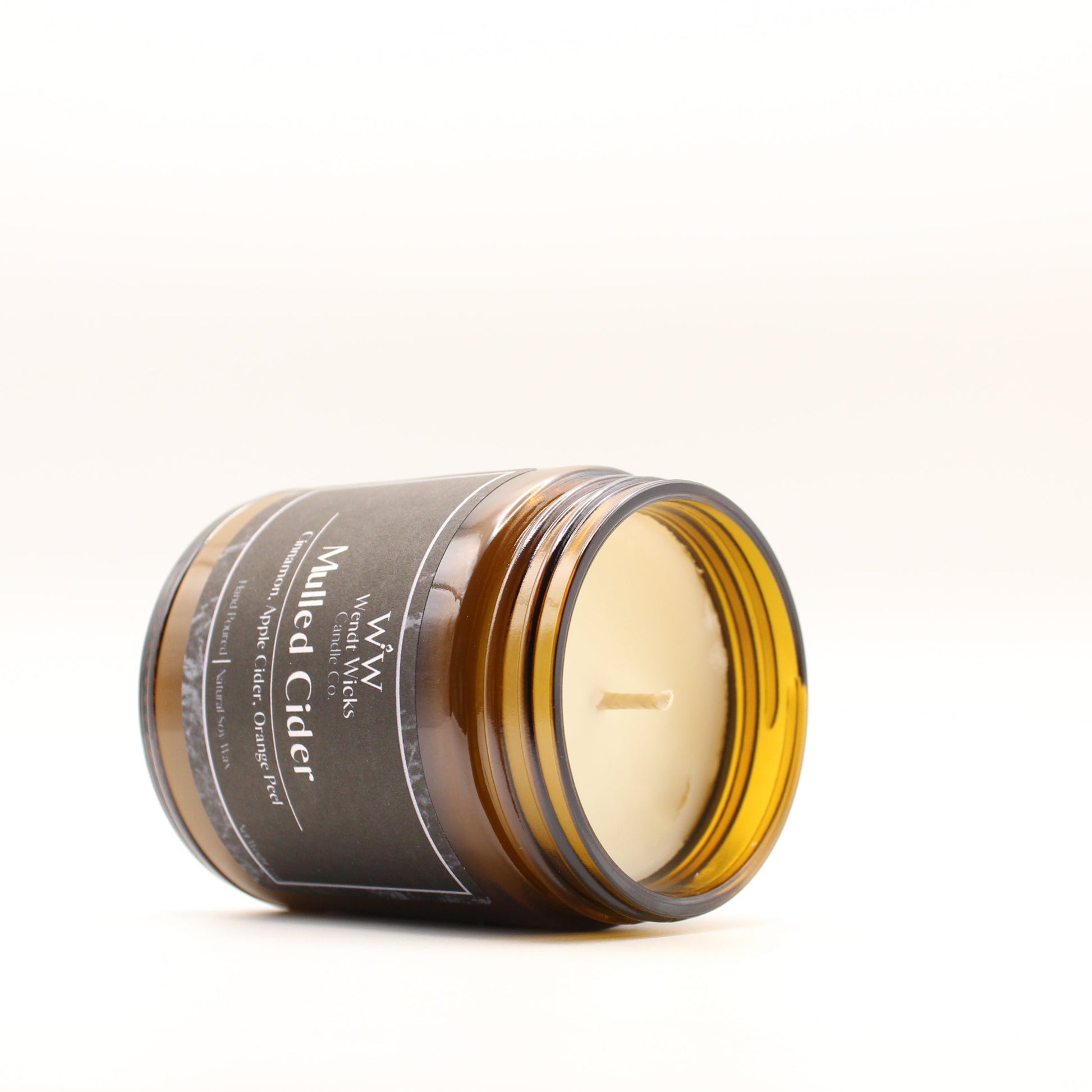 Wendt Wicks amber glass jar candle leaning on its side to show wax and cotton wick. Candle labeled 'Mulled Cider' on a white background