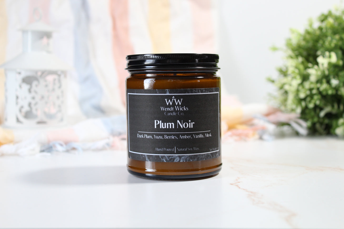 Wendt Wicks Plum Noir candle jar on a white surface with a blurred background