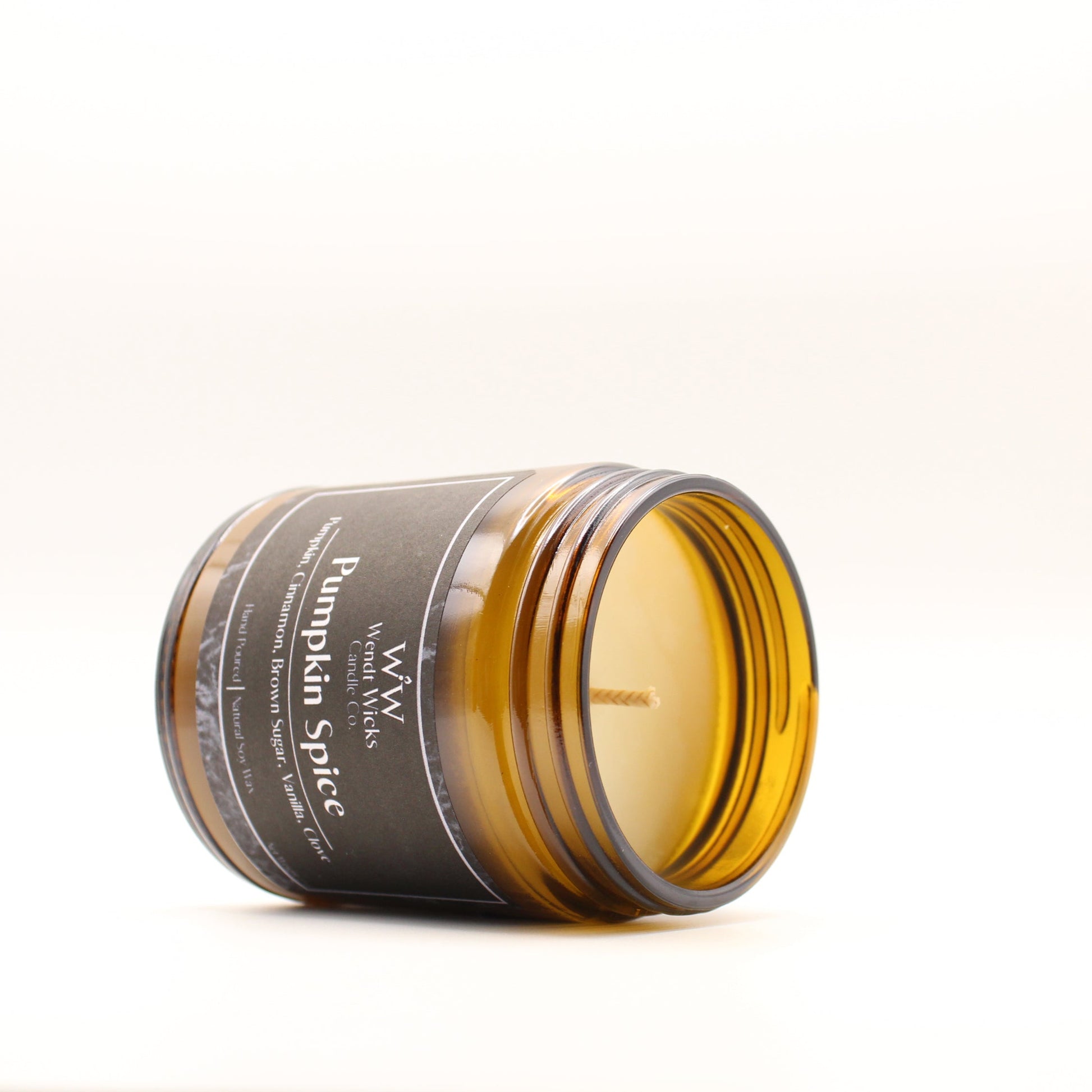 Wendt Wicks amber glass jar candle laying on its side to showcase wax and cotton wick. Candle labeled 'Pumpkin Spice' on a white background